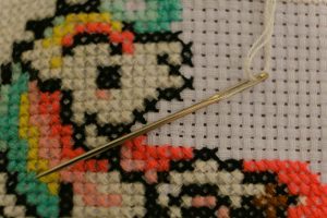 Needle resting across colorful cross stitches and the open grid of white Aida